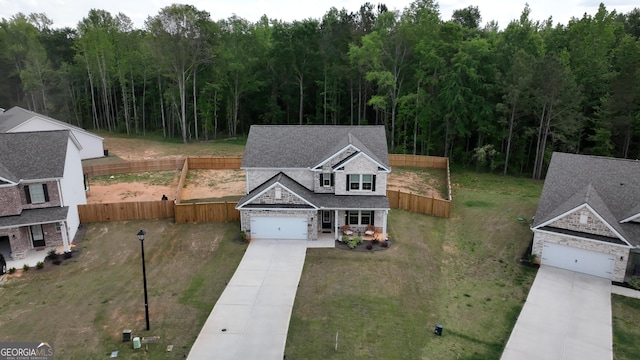 view of front of property featuring a front yard, fence, a wooded view, concrete driveway, and stone siding