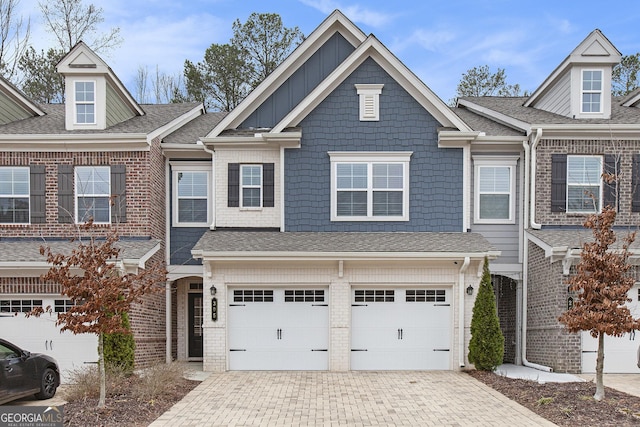 view of property featuring brick siding, decorative driveway, an attached garage, and a shingled roof