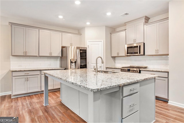 kitchen featuring visible vents, a kitchen island with sink, a sink, gray cabinetry, and stainless steel appliances