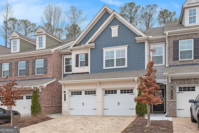 multi unit property with a garage, decorative driveway, brick siding, and a shingled roof