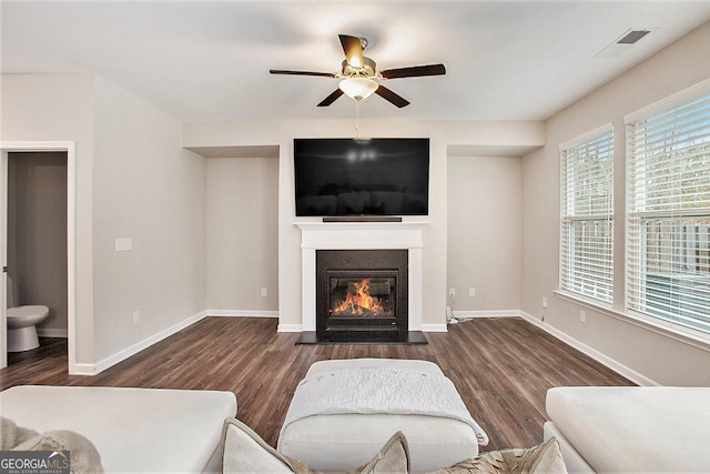 living area with ceiling fan, visible vents, a fireplace with flush hearth, and wood finished floors