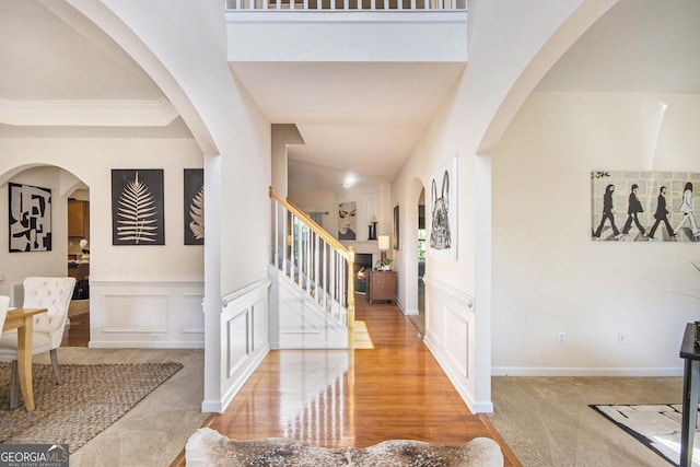 entrance foyer with arched walkways, a wainscoted wall, stairway, and a decorative wall
