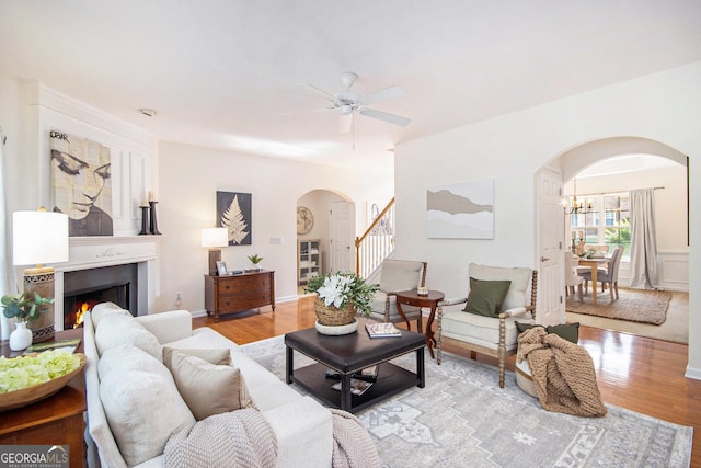 living room with arched walkways, ceiling fan, wood finished floors, and a warm lit fireplace