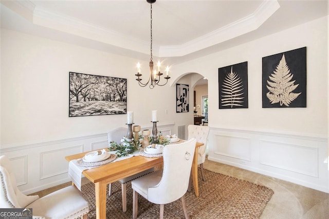 dining area with crown molding, arched walkways, a decorative wall, and a tray ceiling
