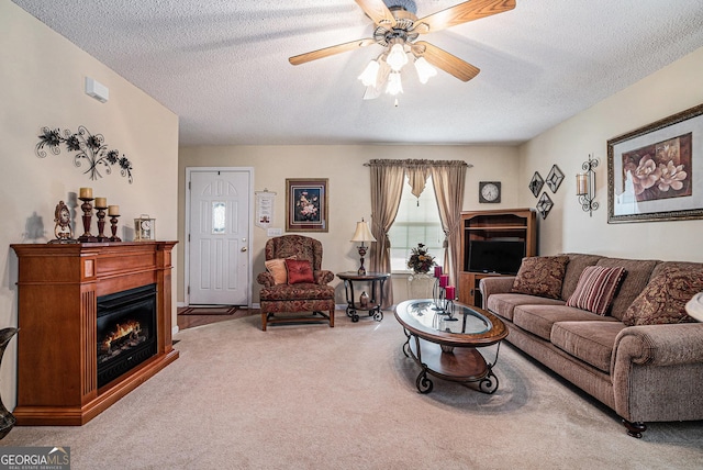 carpeted living room featuring a glass covered fireplace, a ceiling fan, and a textured ceiling