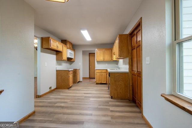 kitchen with white microwave, a sink, light countertops, baseboards, and light wood-type flooring