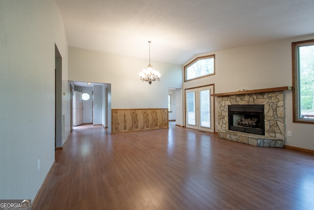 unfurnished living room with a stone fireplace, wood finished floors, a notable chandelier, and vaulted ceiling