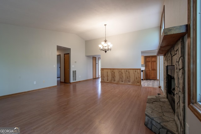 unfurnished living room with light wood-style floors, lofted ceiling, a stone fireplace, and an inviting chandelier