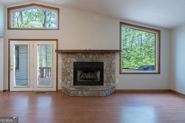 unfurnished living room with a stone fireplace, wood finished floors, and a wealth of natural light