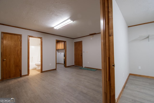 below grade area with a textured ceiling, baseboards, ornamental molding, and light wood finished floors