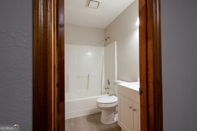 bathroom with a textured wall, vanity, shower / bathtub combination, toilet, and wood finished floors