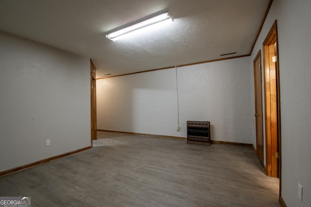 finished basement featuring a textured ceiling, heating unit, wood finished floors, and visible vents