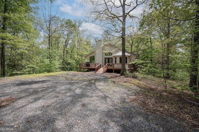 exterior space with a wooded view, a wooden deck, and a chimney