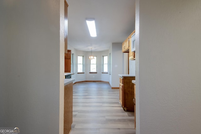 hallway with baseboards, a textured wall, a chandelier, and light wood-style flooring