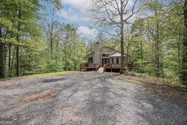 view of front facade with a view of trees, a chimney, and a wooden deck
