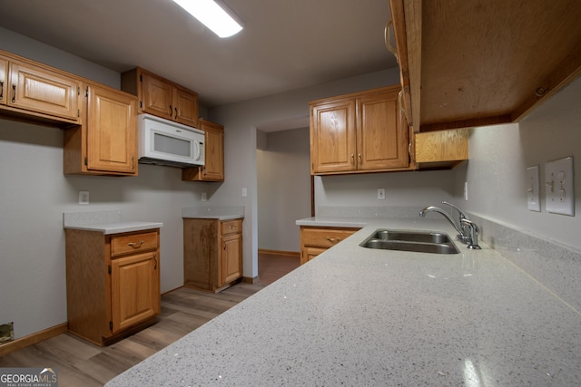 kitchen with a sink, white microwave, brown cabinets, and light wood-style flooring