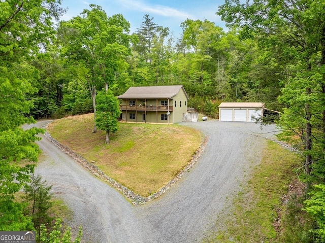 view of front of house featuring a detached garage, a wooden deck, a front yard, an outbuilding, and a forest view