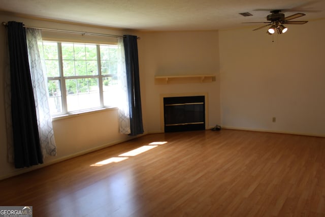 unfurnished living room featuring a ceiling fan, visible vents, a glass covered fireplace, and wood finished floors