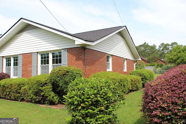 view of home's exterior featuring brick siding, roof with shingles, and a lawn