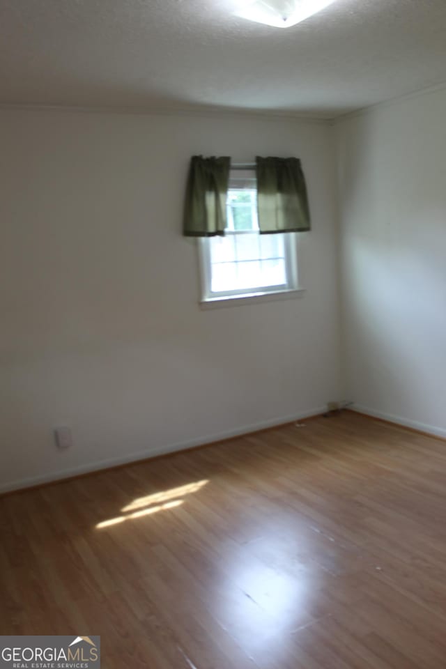 empty room featuring crown molding, baseboards, and wood finished floors