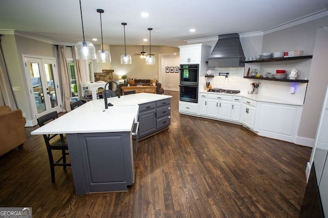 kitchen featuring dobule oven black, stainless steel gas cooktop, open floor plan, an island with sink, and custom range hood