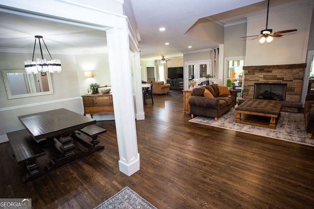 living room featuring ornamental molding, a stone fireplace, ceiling fan with notable chandelier, and wood finished floors