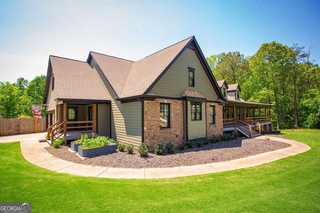 view of side of property featuring fence, covered porch, stone siding, a shingled roof, and a yard