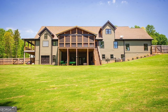 rear view of house with stairway, a lawn, fence, and a sunroom