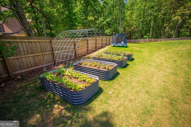 view of yard with a fenced backyard, a view of trees, a trampoline, and a vegetable garden
