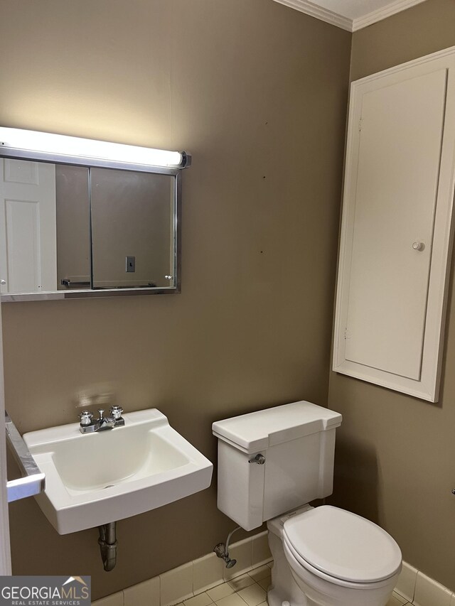bathroom featuring ornamental molding, toilet, baseboards, tile patterned floors, and a sink