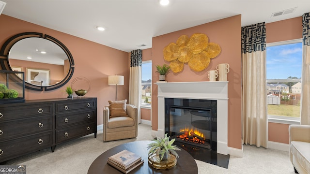 sitting room with visible vents, a glass covered fireplace, a healthy amount of sunlight, and light colored carpet