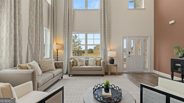 living room with plenty of natural light, baseboards, a towering ceiling, and wood finished floors