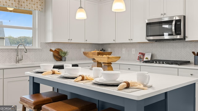kitchen featuring white cabinets, stainless steel microwave, a sink, and a kitchen bar