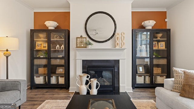 living area with crown molding, baseboards, a fireplace with flush hearth, and wood finished floors