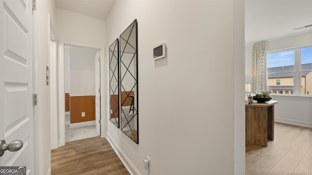 hall featuring baseboards, light wood-style flooring, and visible vents
