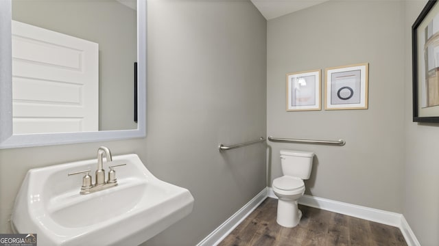 half bathroom with a sink, baseboards, toilet, and wood finished floors