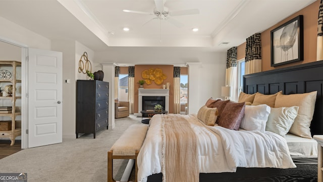 bedroom with light carpet, a glass covered fireplace, recessed lighting, a tray ceiling, and ornamental molding