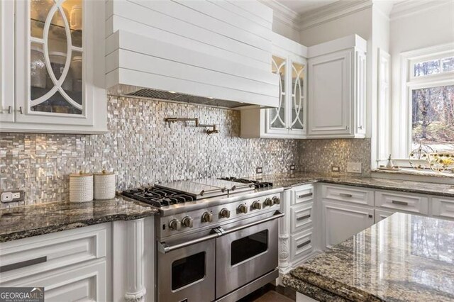 kitchen with glass insert cabinets, premium range hood, white cabinets, range with two ovens, and backsplash