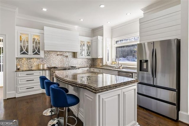 kitchen featuring white cabinets, a sink, a center island, stainless steel appliances, and glass insert cabinets