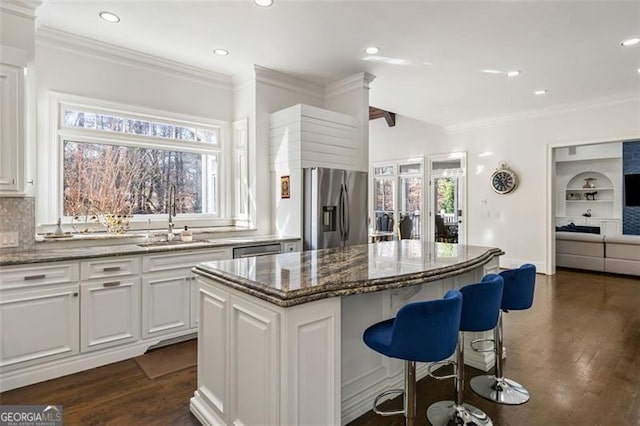 kitchen with ornamental molding, dark wood-style flooring, a kitchen island, a sink, and stainless steel appliances