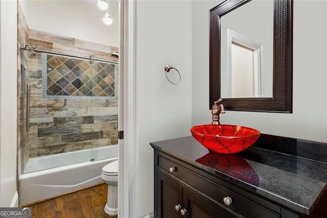 bathroom with toilet, wood finished floors, bath / shower combo with glass door, and vanity