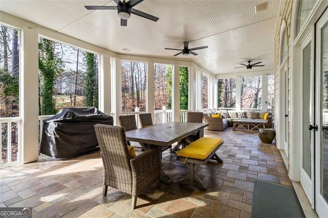 sunroom featuring a ceiling fan, outdoor dining space, and stone tile flooring