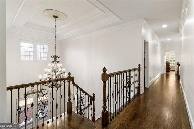 corridor with crown molding, a notable chandelier, wood finished floors, baseboards, and an upstairs landing