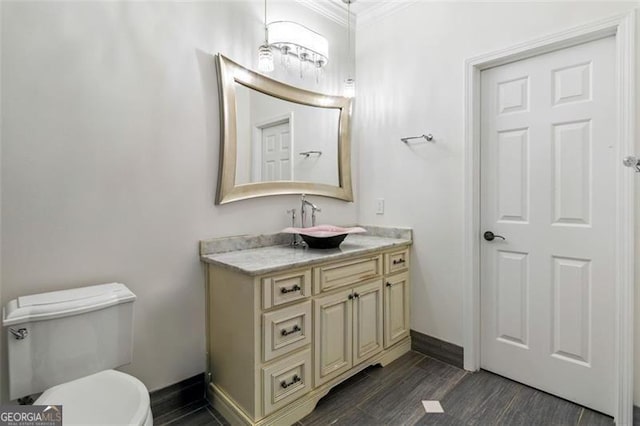 half bathroom with crown molding, wood finished floors, baseboards, vanity, and toilet