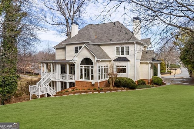back of house featuring a standing seam roof, a chimney, roof with shingles, a lawn, and stairway
