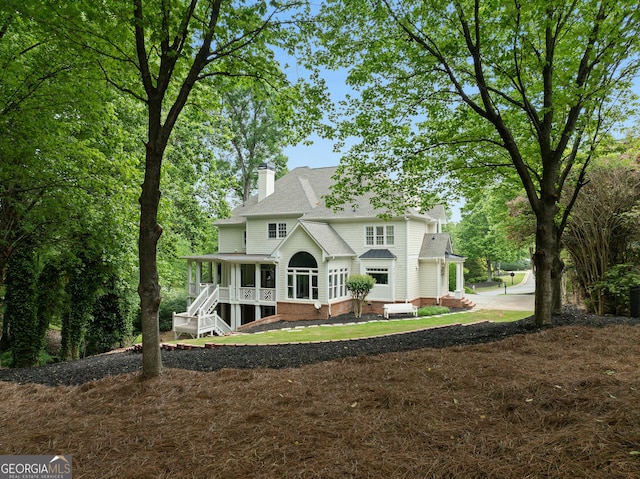 rear view of property with a porch, a lawn, a chimney, and a shingled roof