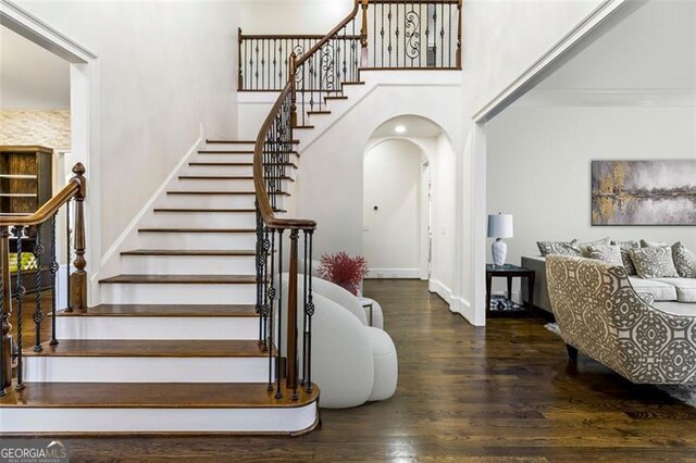 foyer featuring arched walkways, stairs, wood finished floors, and a towering ceiling