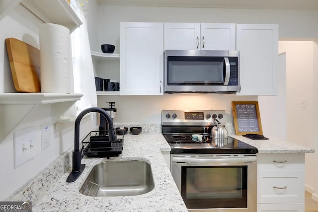 kitchen with appliances with stainless steel finishes, a sink, open shelves, white cabinetry, and light stone counters
