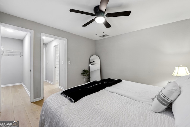 bedroom with a walk in closet, light wood-style floors, baseboards, visible vents, and a closet
