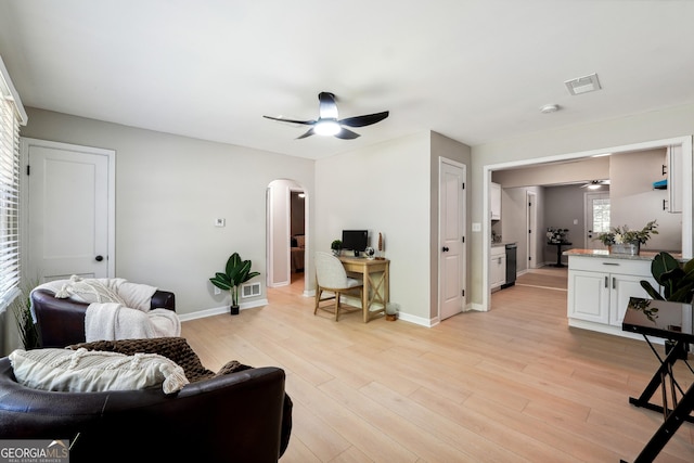 living area with arched walkways, ceiling fan, baseboards, and light wood-style flooring